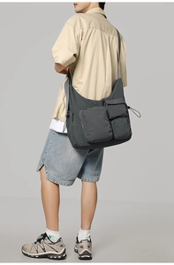 Detail view of dark grey large messenger bag with multiple pockets worn by male model