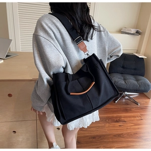 Detail of a black canvas tote bag with brown leather accents and adjustable strap for commuting