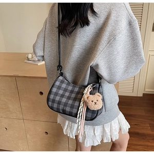 Close-up of black checkered underarm bag with cute plush bear charm on a model
