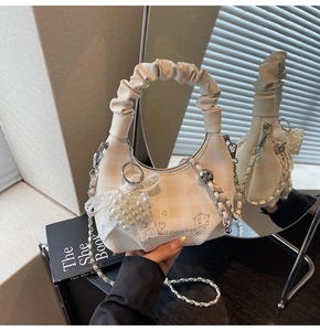 Close-up of cream plaid crossbody bag featuring bear embroidery and pearl heart pendant
