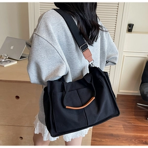 Detail of black canvas tote bag with brown leather accents and multi-pocket design