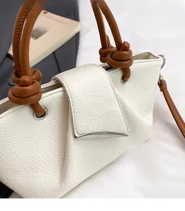 Close-up of white lychee leather bag with knotted brown handle and silver metal clasp