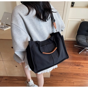 Detail of black canvas tote bag showing brown leather handles and adjustable shoulder strap