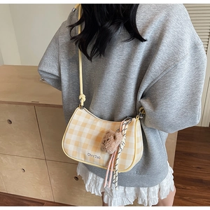Detail of yellow checkered hobo bag with plush bear charm and rope accent in street style