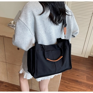 Detail of black canvas tote bag showing brown leather straps and front pockets on model