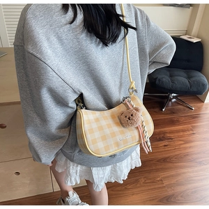 Detail view of yellow plaid shoulder bag with plush bear charm on a female model