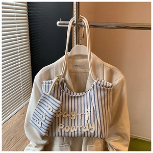 Detailed view of striped canvas tote bag with letter embroidery and a mini charm pouch