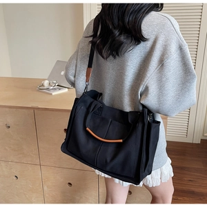 Detail of black canvas tote bag with brown leather handles and adjustable shoulder strap