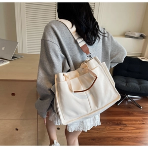 Detail of canvas tote bag with brown leather handles and adjustable shoulder strap