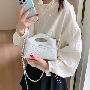 Detail der weißen gesteppten Mini-Tasche mit Strass und Silberschleife auf weißer Jacke