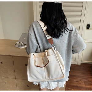 Detail of canvas tote bag with brown leather handles and adjustable shoulder strap