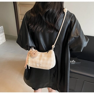 Close-up of beige plaid shoulder bag with stylish plush bear pendant on model