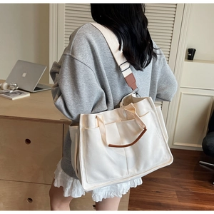 Detail of white canvas tote bag with front pockets and brown leather handle accents