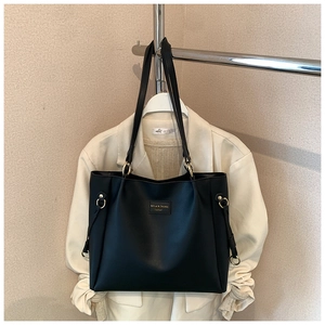 Dettaglio di borsa tote in pelle nera con placca dorata del brand e hardware in metallo