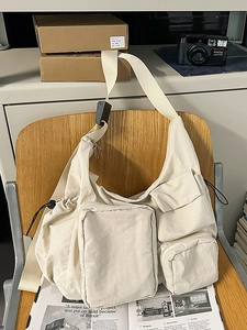 Creamy beige vintage crossbody messenger bag with multi-pocket utility design on a chair