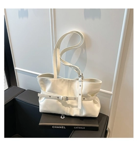 Détail d'un sac cabas en cuir blanc avec plis et boucle sur un fond de livre élégant