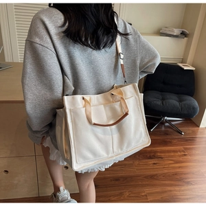 Detail of a large beige canvas tote bag with brown leather handles worn by a model