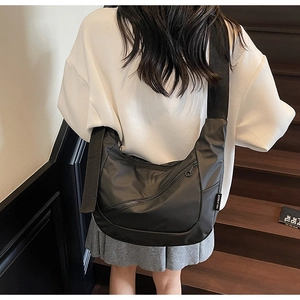Detail of black crescent crossbody bag with wide strap and side brand label shown on model