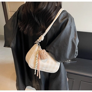 Detailed view of checkered shoulder bag with bear plush charm and woven tassel