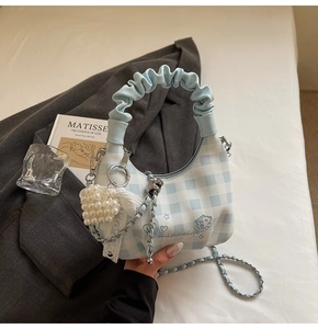Detail of light blue checkered hobo bag with pearl heart charm and chain strap