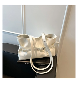 Détail du grand sac cabas crème avec boucle décorative posé sur un siège en cuir foncé