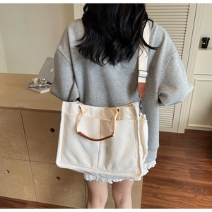 Detailed back view of a white canvas tote bag with leather straps on a model in a cozy room