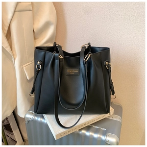 Dettaglio di una borsa tote nera in pelle con anelli metallici e logo su sfondo curato