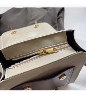 Close-up of smooth golden metal zipper and beige brown textured leather bag flap