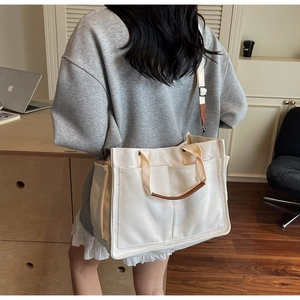 Detail of white canvas tote bag with functional outer pockets and brown leather handles