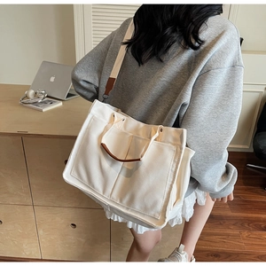 Detail of white canvas tote bag showing functional front pockets and brown leather straps