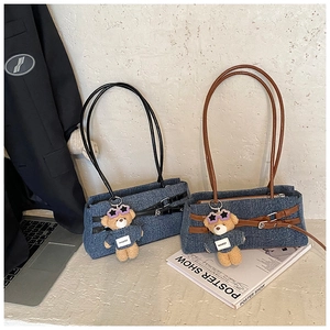 Detail of denim patchwork tote bag with leather belt accents and plush bear charm