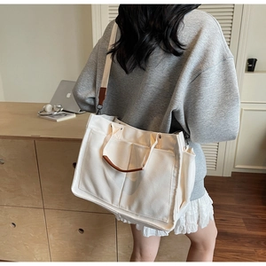 Detail of off-white canvas tote bag featuring brown leather handles and multi-pocket design