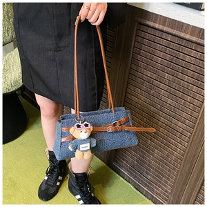 Detail of blue denim baguette bag with brown leather straps and cute bear charm pendant