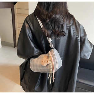 Detail of grey checkered baguette bag with bear charm and tassel on a model shoulder