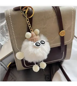 Detail of white plush pompom charm with pink hat and big eyes on a two-tone backpack