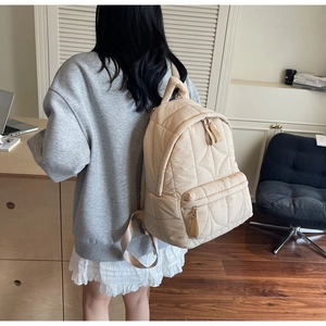 Detail of a beige quilted backpack featuring large wave patterns and a spacious front pocket
