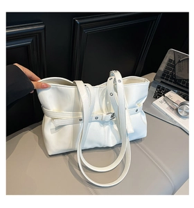 Détail d'un sac cabas blanc avec boucle de ceinture et œillets argentés sur coussin gris