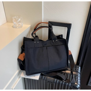 Detail of black canvas tote bag with brown leather handles on a travel suitcase