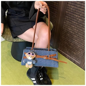 Detailed view of denim shoulder bag with brown leather straps and a cute bear charm