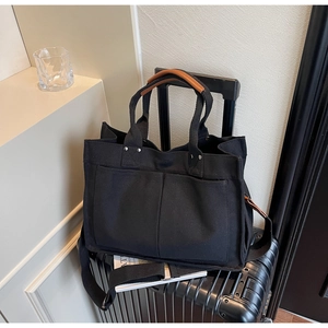 Detail of black canvas tote bag with brown leather handles placed on luggage