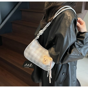 Detail of grey checkered underarm bag with knot strap and plush bear charm decoration