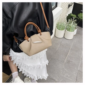 Close-up of beige lychee grain bucket bag featuring a brown twisted handle and silver buckle
