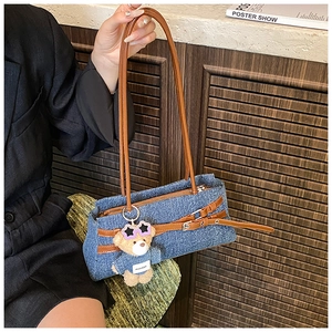 Detail of blue denim shoulder bag with leather straps and cute teddy bear charm