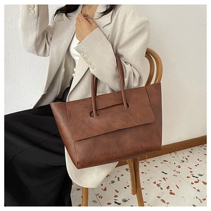 Detailed view of a large vintage brown tote bag being held by a model in a casual setting.