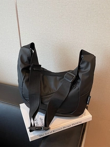 Minimalist matte black nylon tote bag with wide strap on books in a lifestyle setting