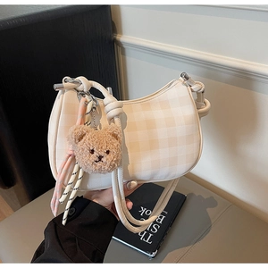Detail of cream checkered hobo bag featuring a plush bear charm and woven decoration