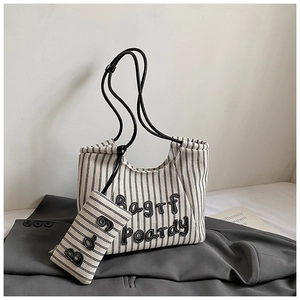 Detail of striped canvas tote bag with black embroidery and shoulder strap on a grey suit