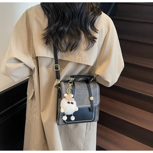 Detail view of retro crossbody bag with plush monster charm on khaki trench coat