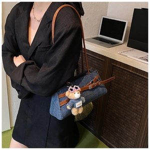 Detail of blue denim baguette bag featuring brown leather straps and cute bear pendant