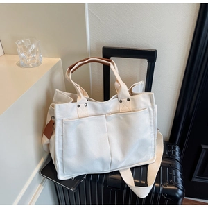 Detail of white canvas tote bag with front pockets and brown leather handle on a suitcase